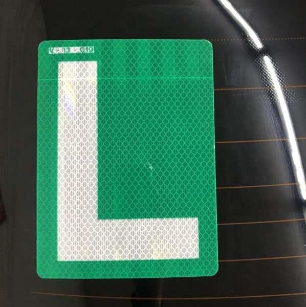 Green and white reflective L sticker displayed on a vehicle rear window