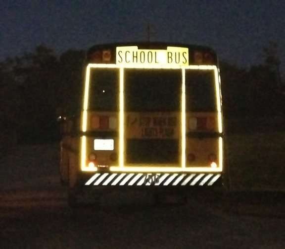 Rear school bus lettering and outline markings under directional light