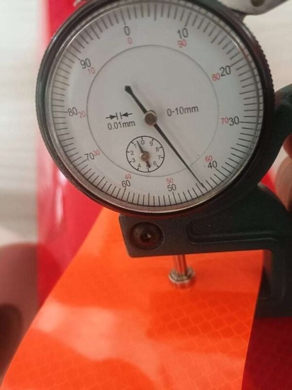 Orange prismatic reflective material close-up with thickness gauge